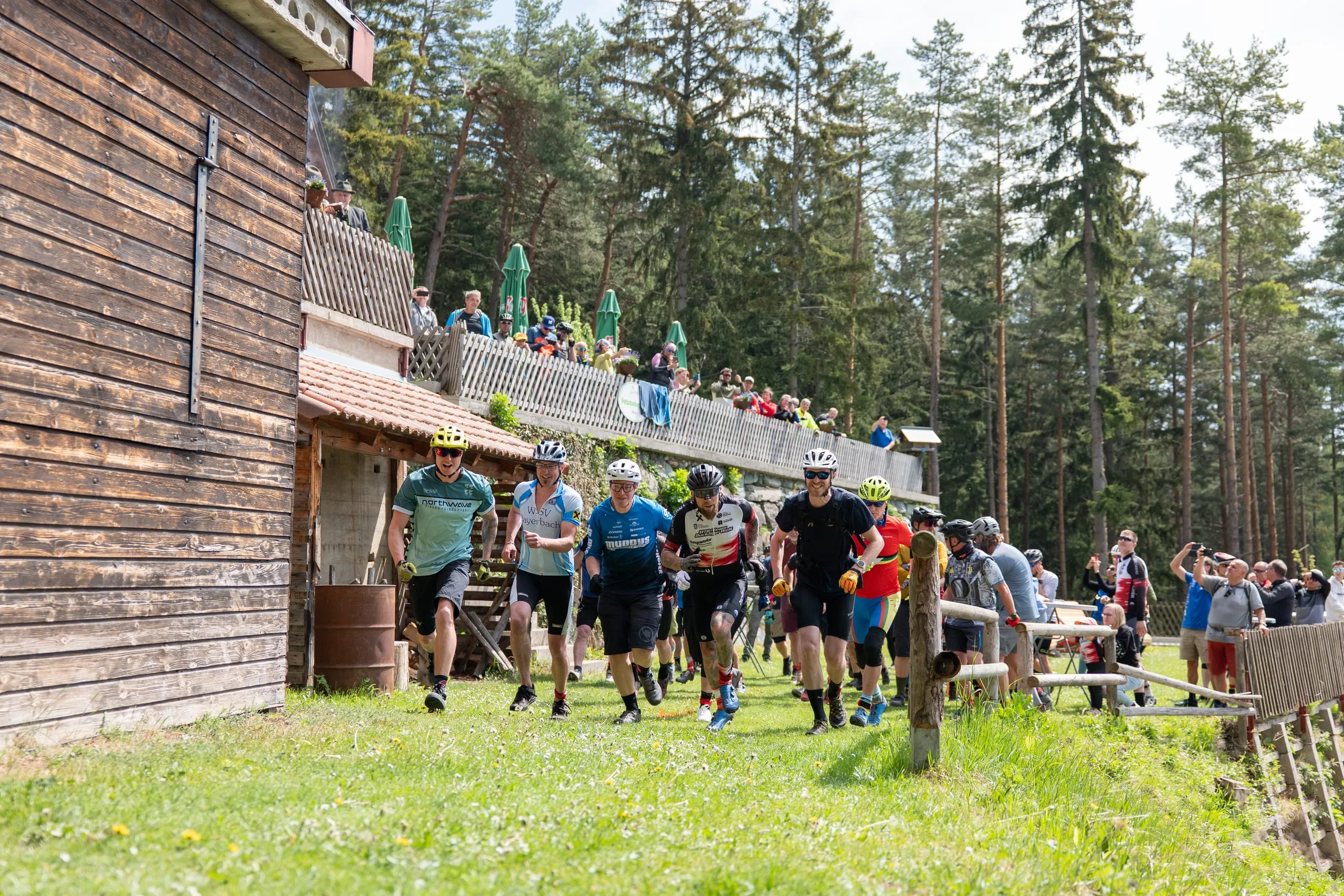 Le-Mans-Start zu Fuß: Fahrerinnen und Fahrer laufen in Radschuhen über die Wiese zu ihren Bikes