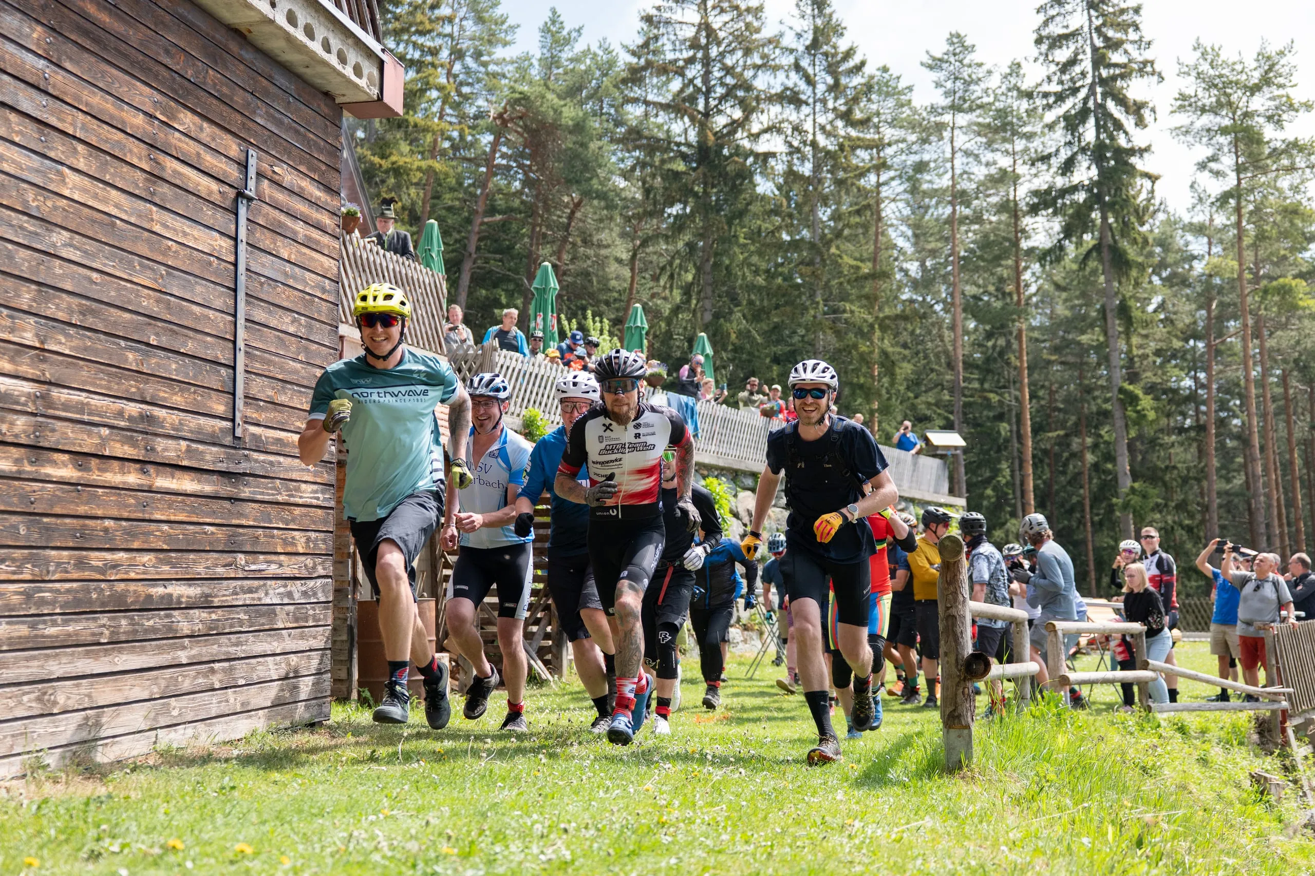 Laufstart an der Hütte: vorne ein Fahrer im mintfarbenen Trikot mit gelbem Helm, dahinter das Feld