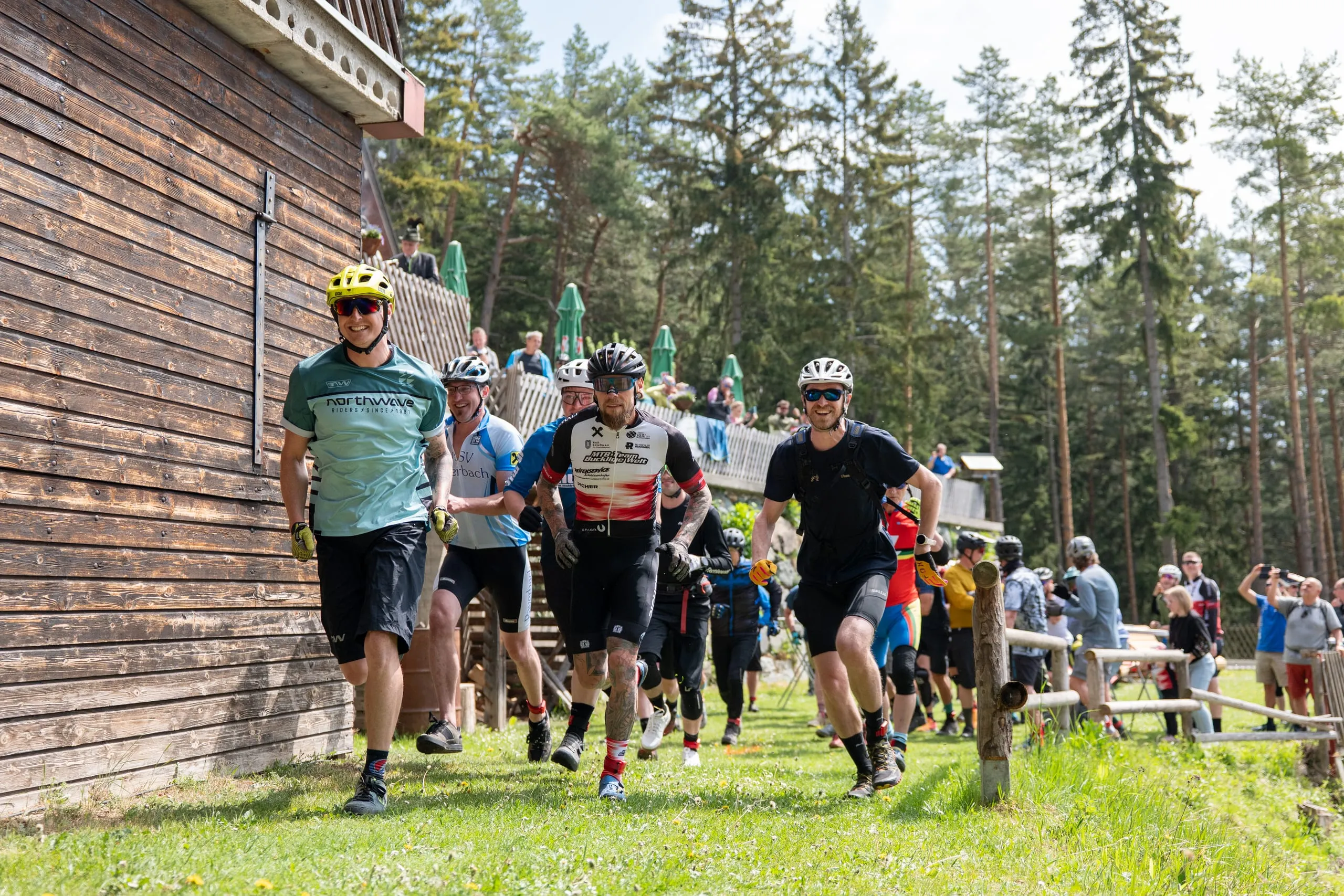 Laufstart an der Hütte: vorne ein Fahrer im mintfarbenen Trikot mit gelbem Helm, dahinter das Feld