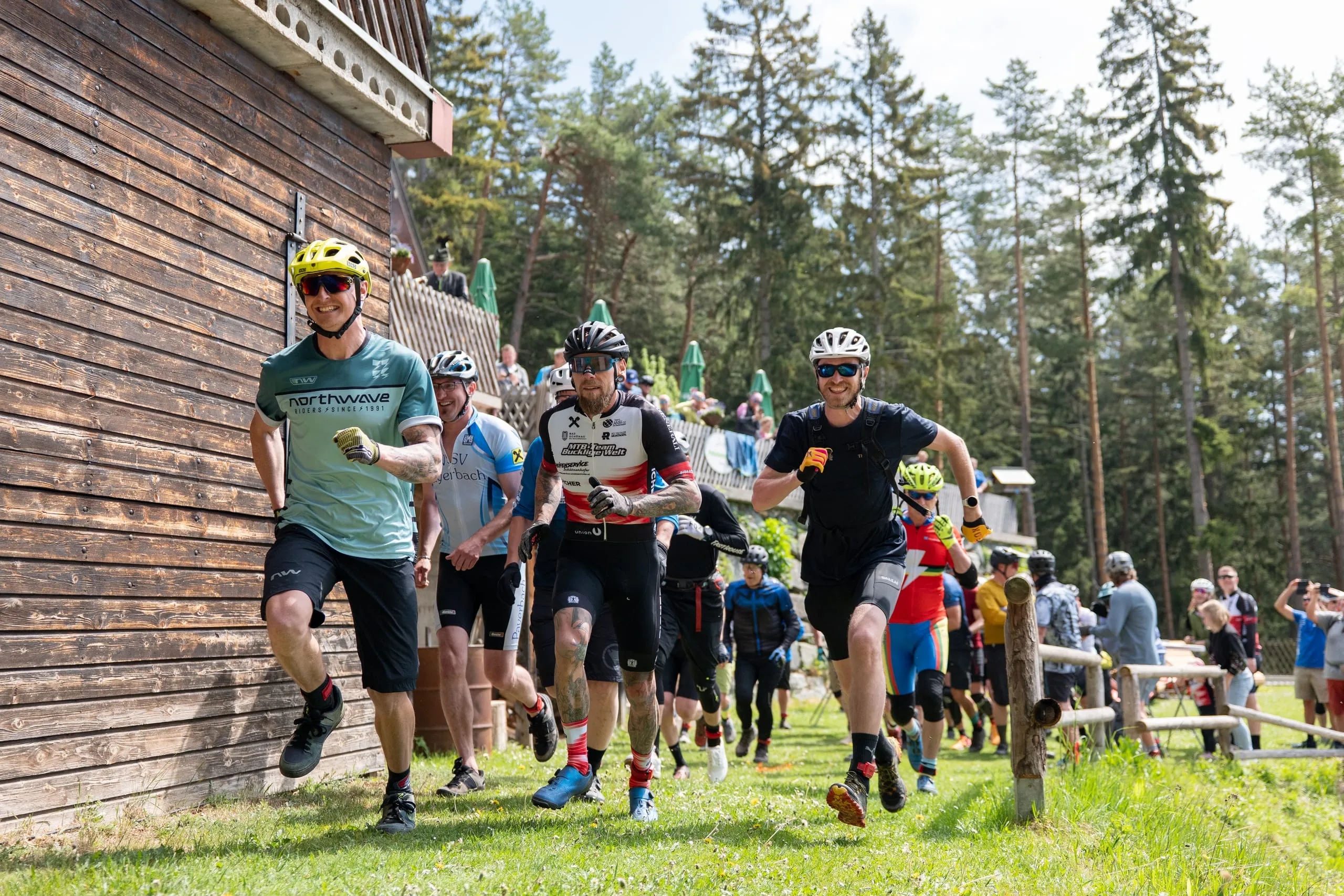 Laufstart an der Hütte: vorne ein Fahrer im mintfarbenen Trikot mit gelbem Helm, dahinter das Feld