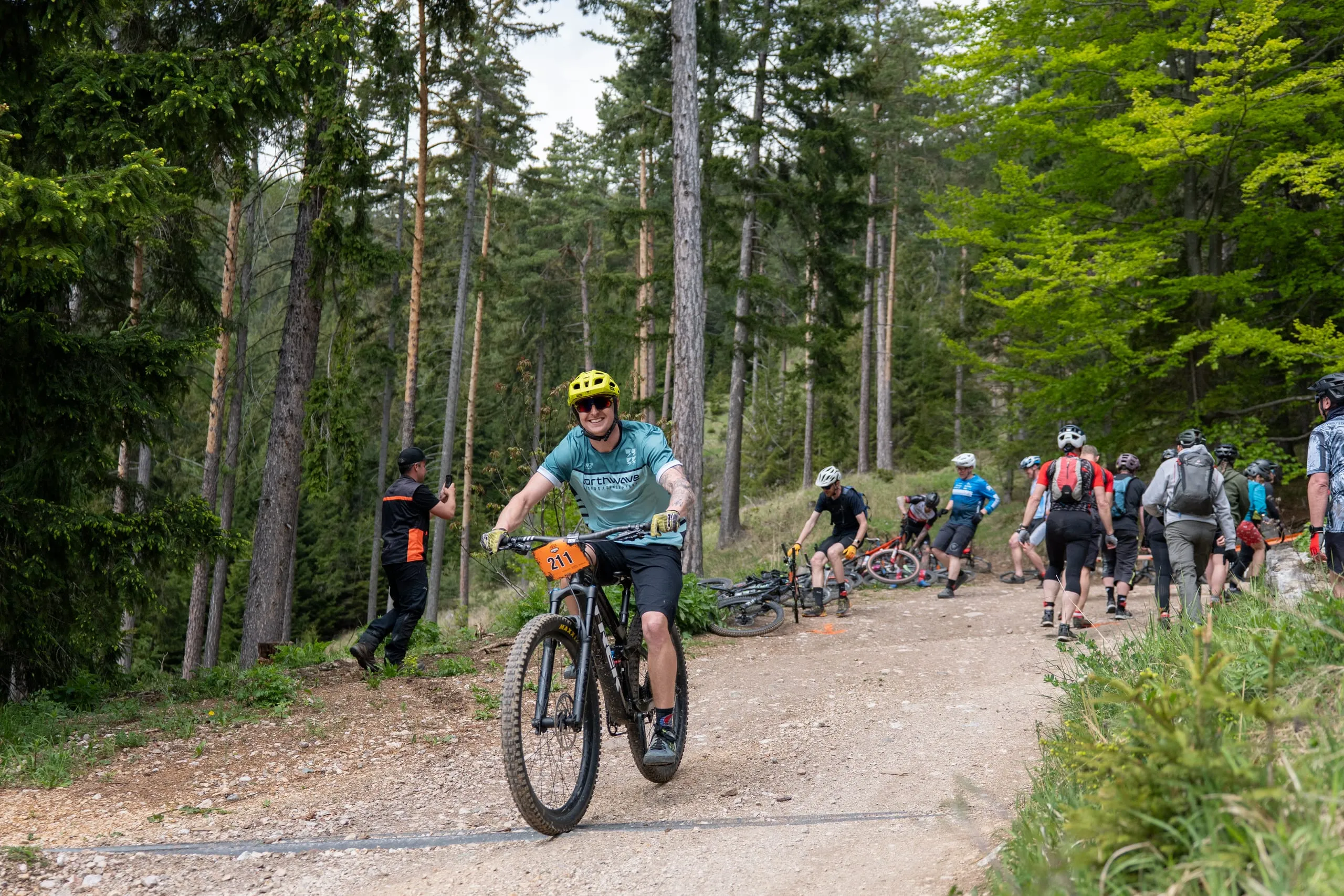 Erste Meter auf dem Rad: ein Fahrer im mintfarbenen Trikot biegt auf den Schotterweg, hinten Wechselzone mit abgelegten Bikes