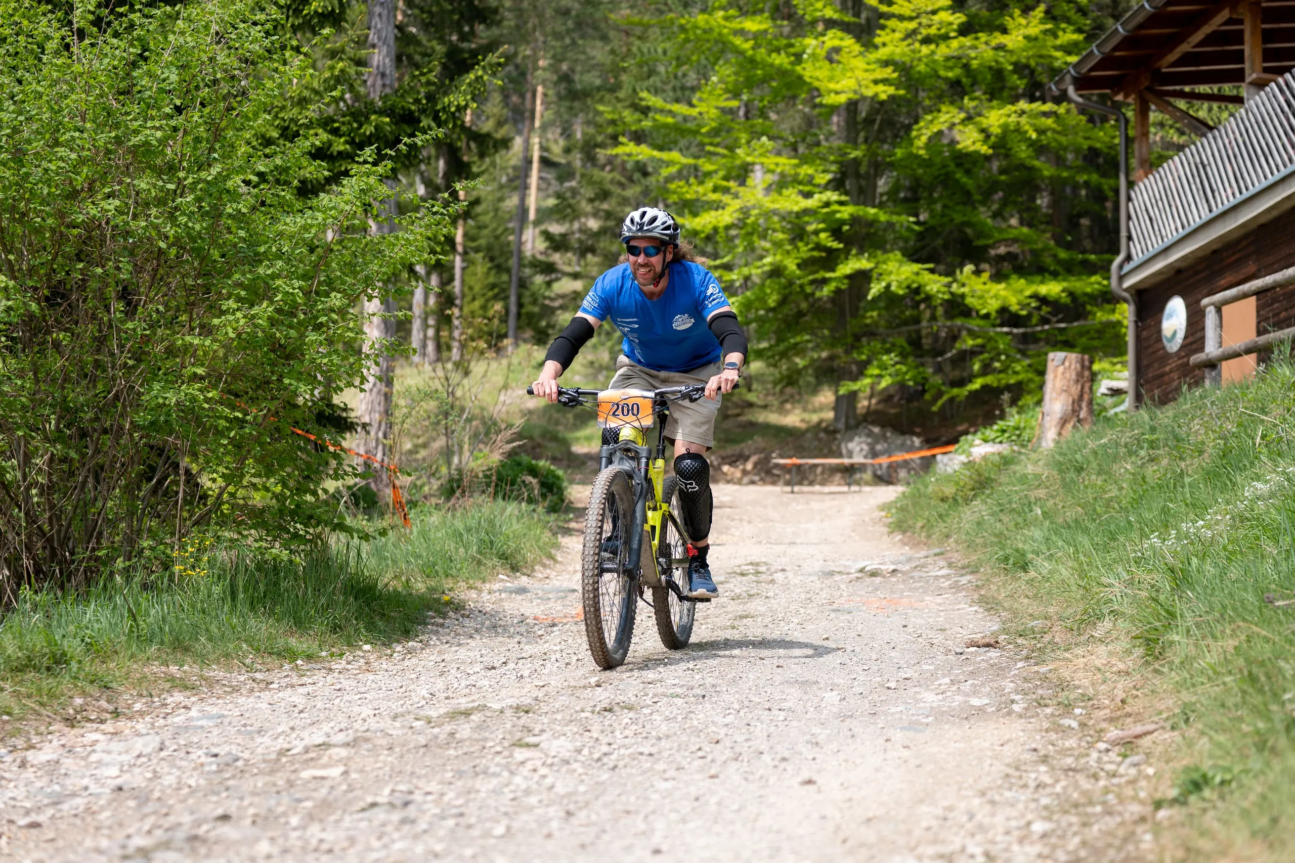 Ein Fahrer im blauen Trikot rollt den Schotterweg vor der Hütte hinunter