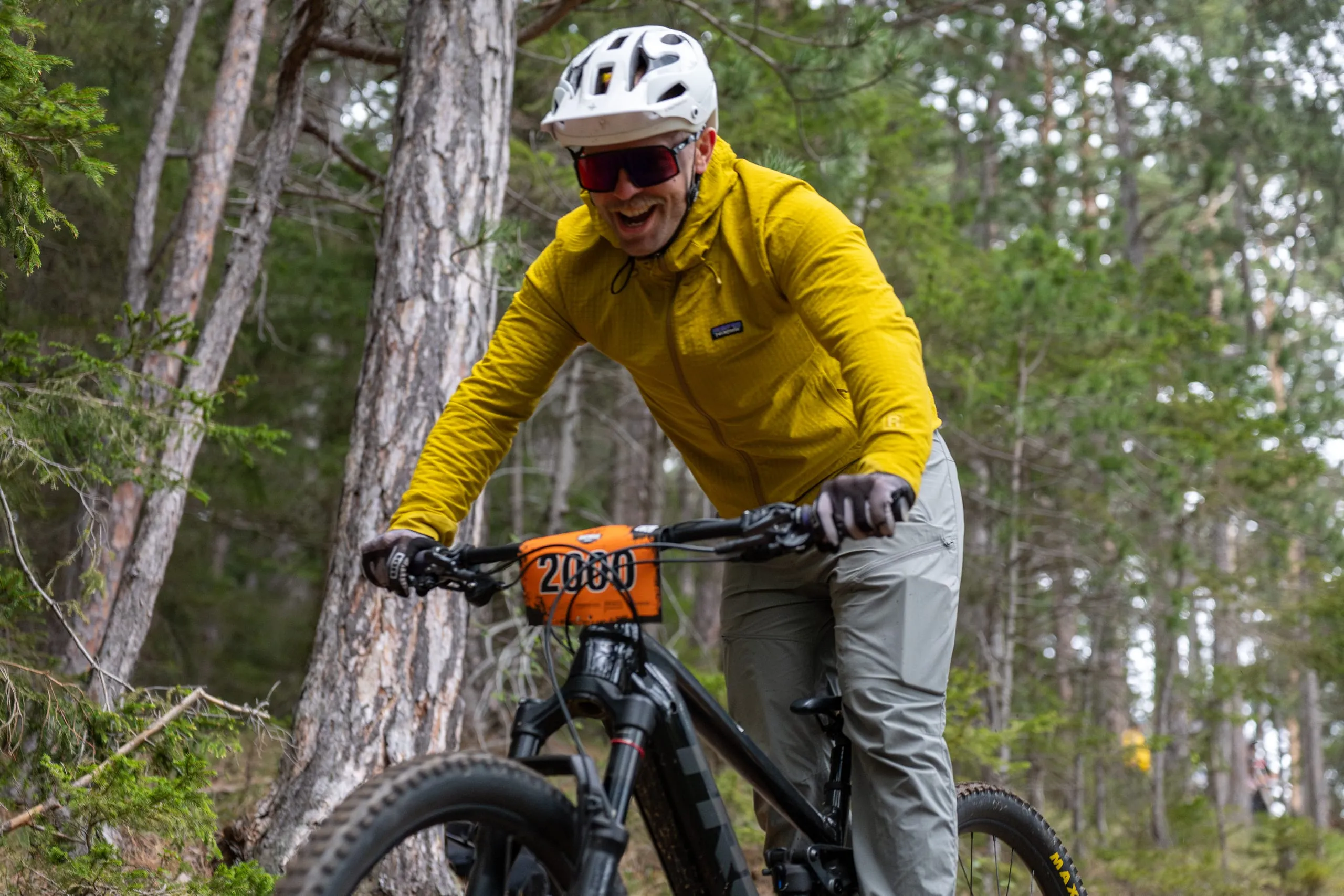 Ein grinsender Fahrer in gelber Jacke auf einem E-Bike, Startnummer am Lenker, ganz nah an der Kamera